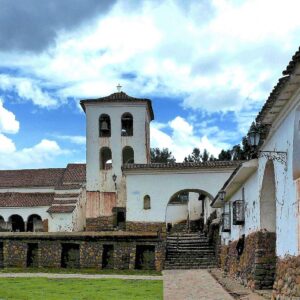 Chinchero: templo colonial blanco con campanario sobre muros incas de piedra con hornacinas, junto a una casona con arcos y un jardín verde