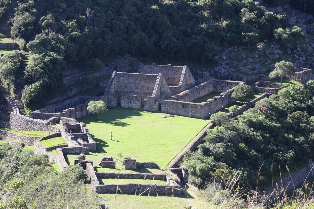 Edificios de piedra inca y una plaza de césped rodeados de bosque, vistos desde arriba en Choquequirao