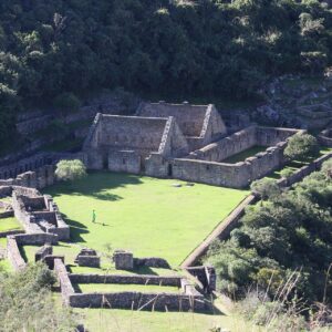 Edificios de piedra inca y una plaza de césped rodeados de bosque, vistos desde arriba en Choquequirao