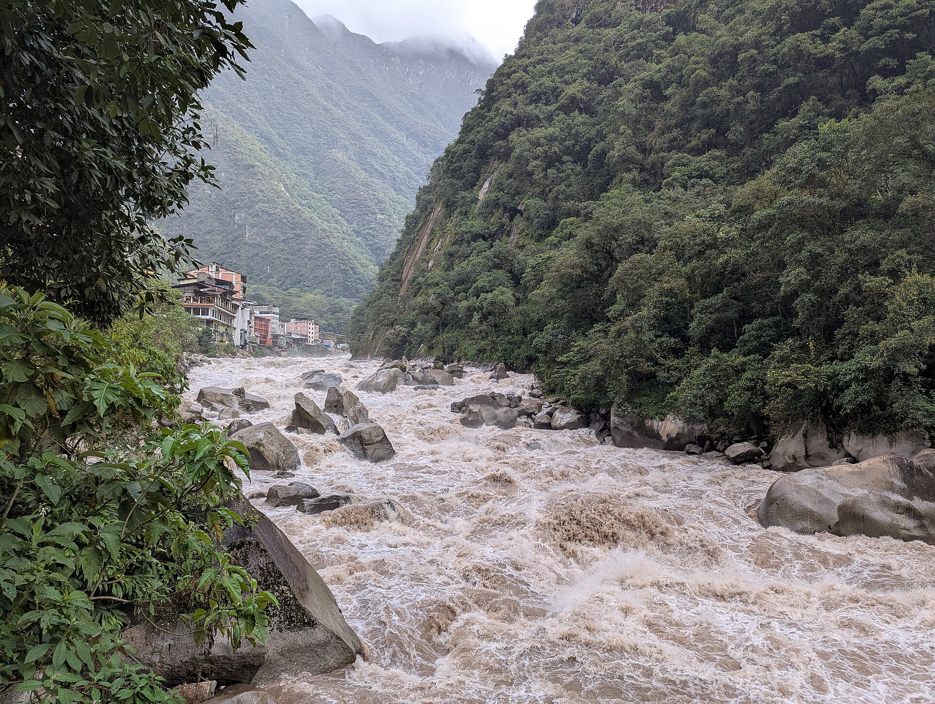 Río Vilcanota, que también pasa junto al museo de sitio de Machu Picchu: aguas turbias entre grandes rocas y laderas de bosque, en Machupicchu Pueblo