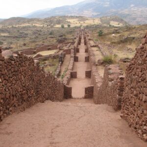 Pikillaqta: calle recta entre altos muros de piedra rojiza sin tallar que baja hacia el valle, con cerros al fondo