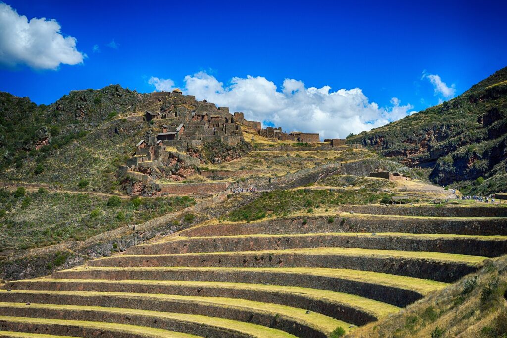Pisac: andenes de piedra en una ladera y, más arriba, las ruinas incas del parque arqueológico, bajo un cielo azul con nubes
