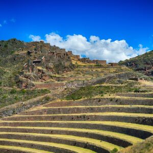Pisac: andenes de piedra en una ladera y, más arriba, las ruinas incas del parque arqueológico, bajo un cielo azul con nubes