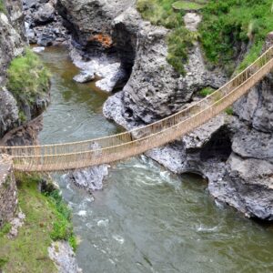Puente Q'eswachaka: puente colgante de cuerdas de paja dorada cruza un río verde entre paredes de roca gris, con bases de piedra a cada lado