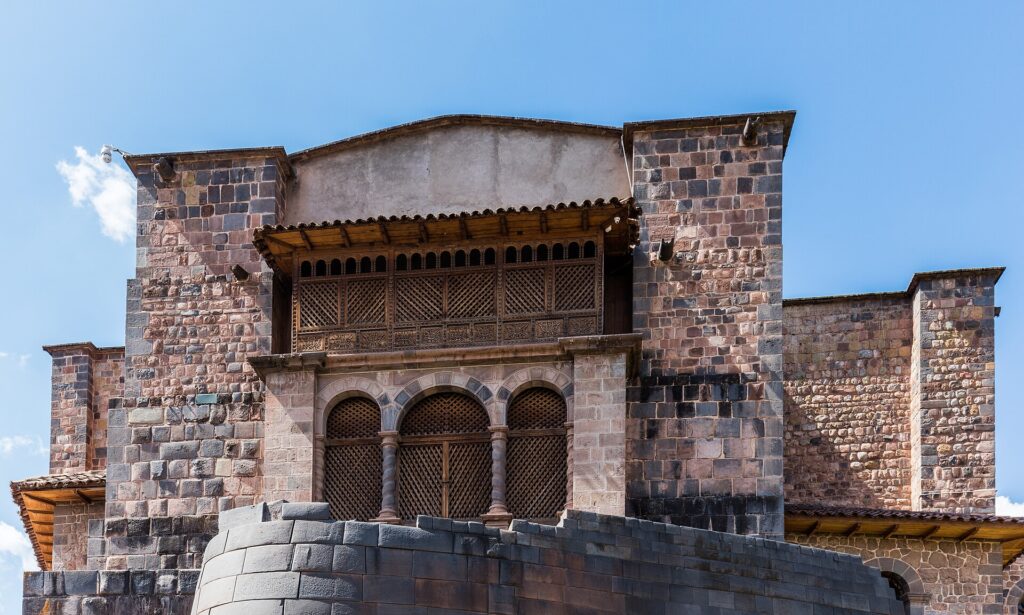 Qorikancha: muro inca curvo de piedra gris bajo el convento colonial con balcón de madera y arcos