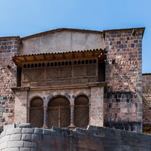 Qorikancha: muro inca curvo de piedra gris bajo el convento colonial con balcón de madera y arcos