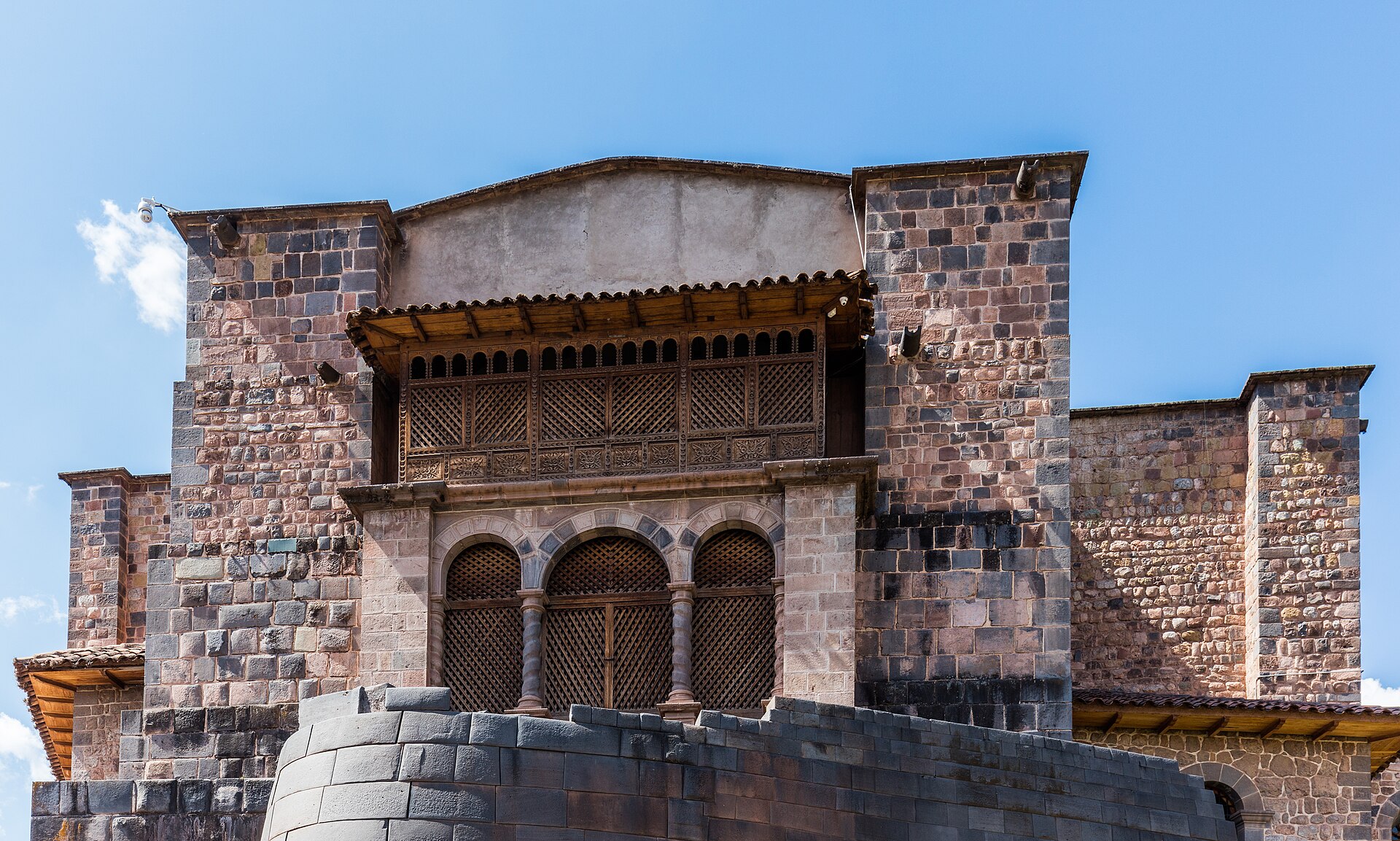 Qorikancha: muro inca curvo de piedra gris bajo el convento colonial con balcón de madera y arcos