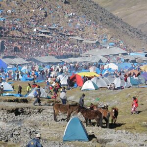 Qoyllur Rit'i: cientos de carpas de colores y peregrinos llenan una ladera de montaña junto al santuario de techo rojo, bajo cerros áridos
