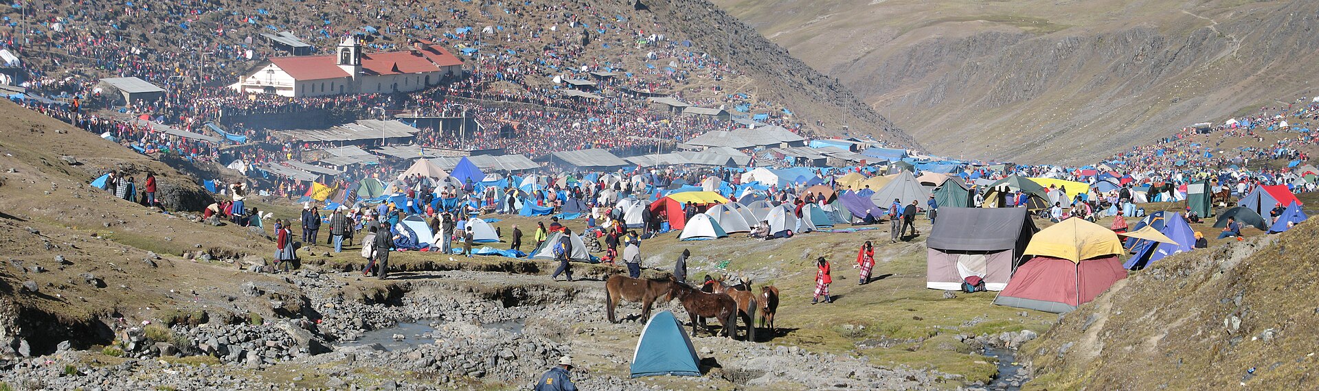 Qoyllur Rit'i: cientos de carpas de colores y peregrinos llenan una ladera de montaña junto al santuario de techo rojo, bajo cerros áridos