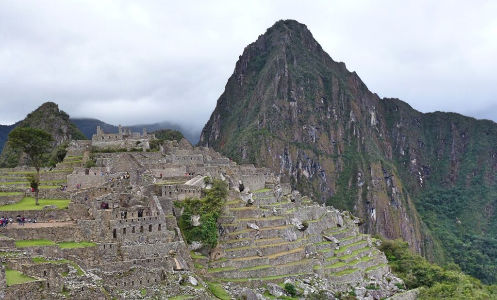 Terrazas de piedra de Machu Picchu bajo cielo parcialmente nublado, con montañas verdes al fondo