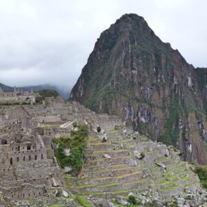 Terrazas de piedra de Machu Picchu bajo cielo parcialmente nublado, con montañas verdes al fondo