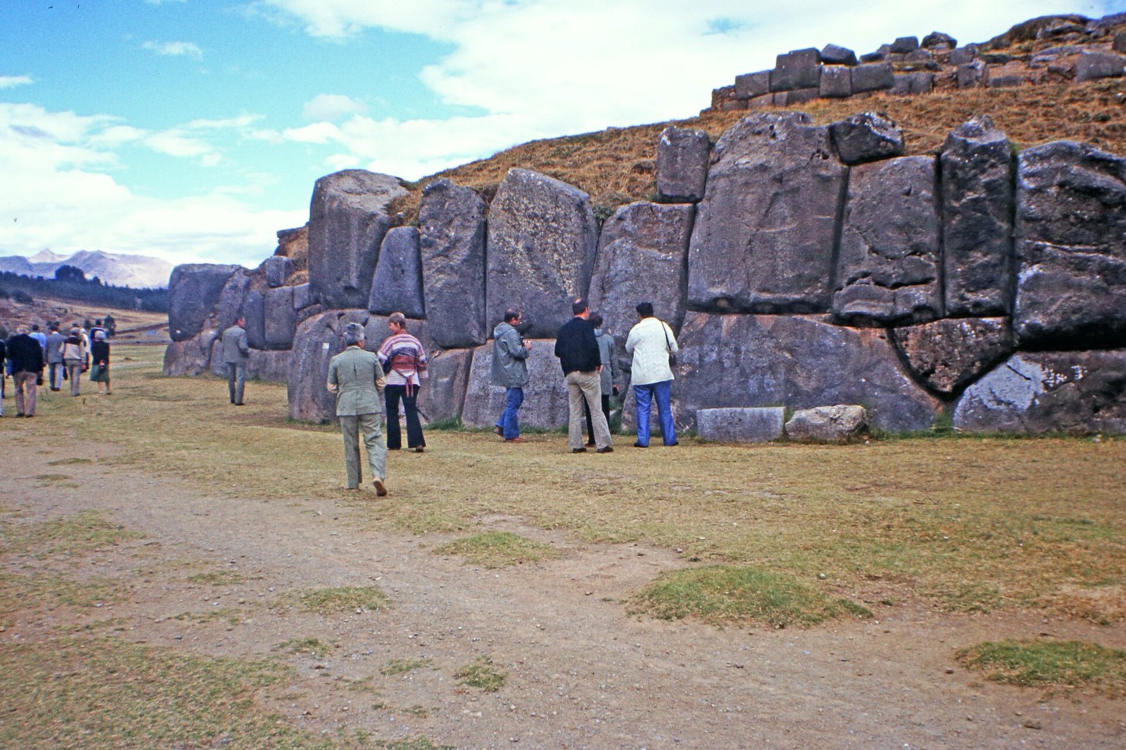 Visitantes junto a los grandes muros de piedra inca de Saqsayhuamán en Cusco bajo cielo azul