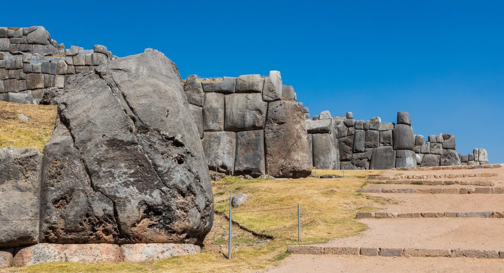Sacsayhuamán: muros incas de enormes bloques de piedra gris en varios niveles, con pasto verde y escalones de piedra bajo un cielo azul