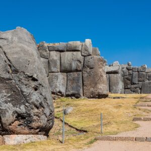 Sacsayhuamán: muros incas de enormes bloques de piedra gris en varios niveles, con pasto verde y escalones de piedra bajo un cielo azul